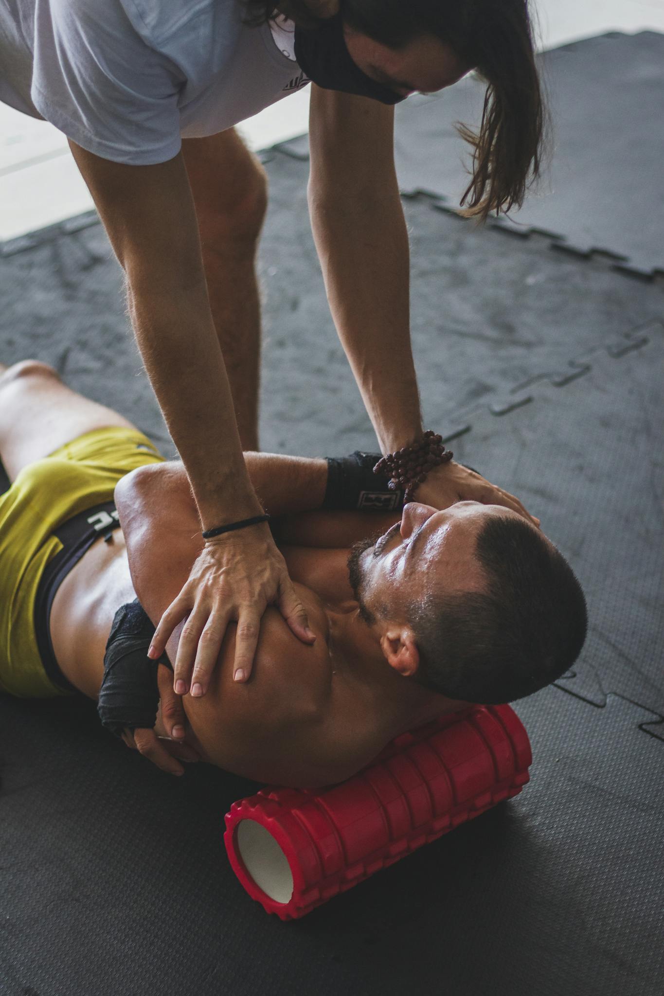 Athlete using a foam roller for muscle stretching with instructor's guidance in a gym setting.