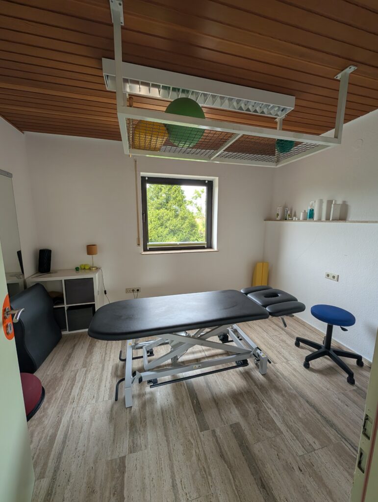 Behandlungsraum mit Therapieliege und Fenster zum Garten